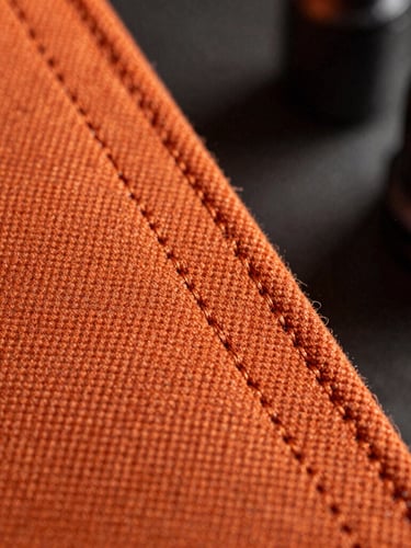 Macro shot of heavy-duty triple-stitched seams on high-denier orange canvas, dramatic cold workshop lighting with steel dust particles in the air