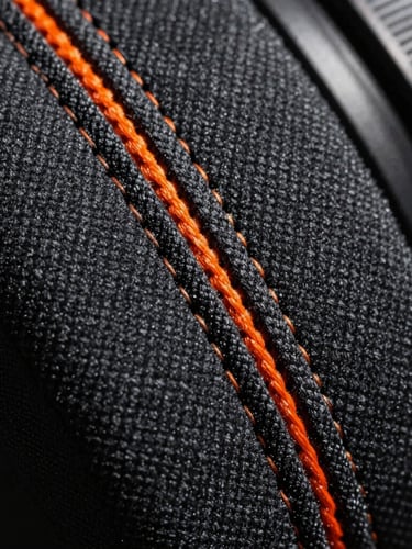 Macro close-up of heavy-duty triple-stitched canvas seam, high-contrast industrial lighting, orange safety thread visible against charcoal fabric