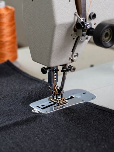 Close-up macro shot of a heavy-duty industrial sewing machine triple-stitching thick charcoal canvas, orange thread, metallic machinery components in sharp focus.