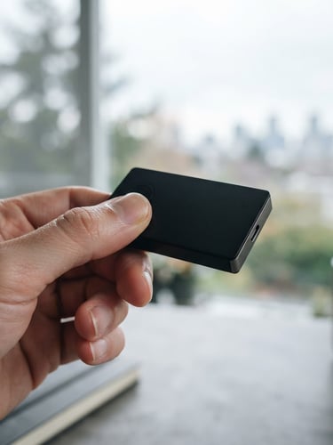 Makroaufnahme einer Hand, die eine matte schwarze Hardware-Wallet hält, im Gegenlicht eines Fensters, auf einem minimalistischen Schreibtisch. Scharfe Tiefenschärfe auf der Wallet. Muted Slate und metallische Töne.