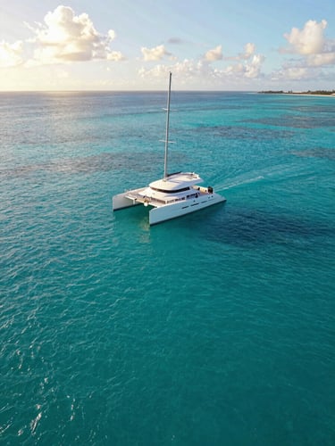 A spacious white catamaran sailing on vibrant turquoise waters under bright Caribbean sunlight, wide-angle environmental shot showing open space and calm seas.