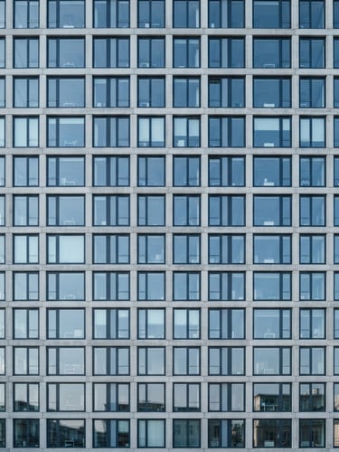 Straight-on architectural view of a modern concrete office building facade with clean grid lines, bright cool-toned daylight