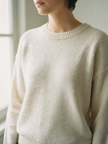 A candid medium-close crop of a model wearing a heavy cream knit sweater, soft diffused window light, 35mm film texture, neutral background