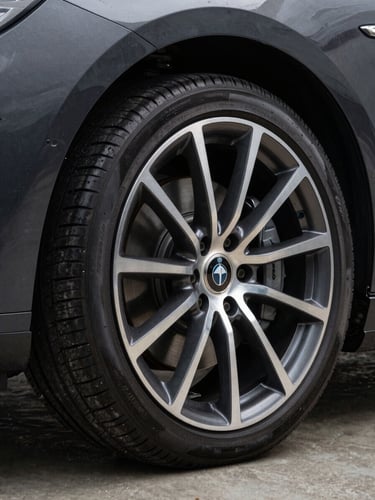 Close-up three-quarter view of a dark luxury alloy wheel on a premium vehicle, studio lighting with matte concrete backdrop, sharp metallic spokes catching a single overhead strobe, deep shadows around the tire wall, magazine-quality product shot