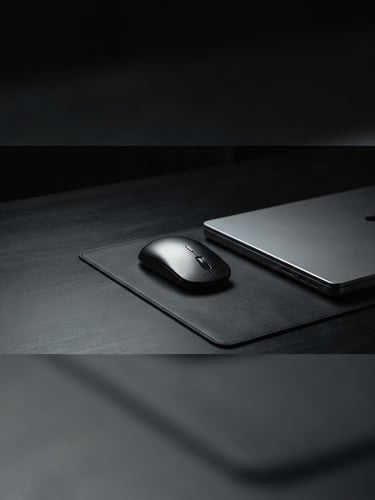 Sleek, minimalist desk setup with a high-performance laptop and a precision-milled mouse, bathed in dramatic low-key studio lighting, sharp focus on the metallic textures, expansive negative space, 21:9 panoramic frame, laptop on the right third, dark charcoal tones.