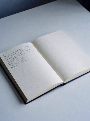 A minimalist desk setup with an open notebook showing handwritten edits, soft overcast daylight, muted paper tones with deep blue shadows, 35mm film grain