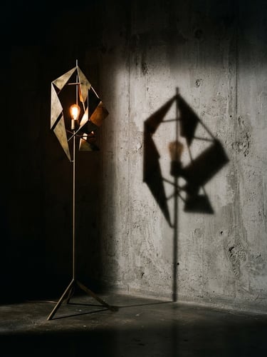 Dramatic high-contrast editorial photography of a tall brass sculptural floor lamp casting a sharp geometric shadow on a raw concrete wall, warm amber glow, 35mm