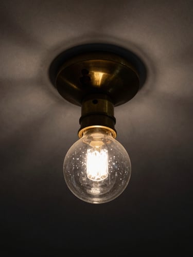 Tight macro shot of a cast brass and hand-blown glass joint on a minimalist ceiling fixture, dramatic chiaroscuro lighting, deep shadows, 35mm