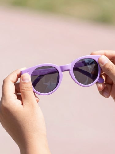 Hands gently flexing a highly flexible lilac children's sunglasses frame, showing playground-proof durability, bright natural light, soft pastel background, macro shot