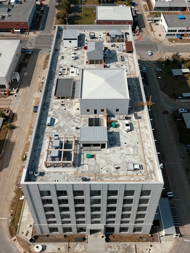 Wide overhead aerial view of a completed commercial building site, straight-down angle showing rooftop detail and surrounding infrastructure, natural midday daylight, precise color rendering with no post-production enhancement