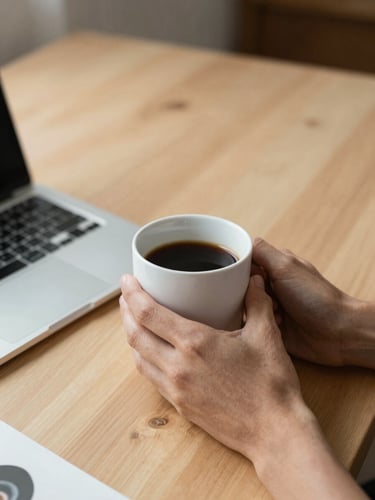 Planos medios de manos sosteniendo una taza de café caliente sobre un escritorio de madera clara y ordenado, luz natural suave de mañana.