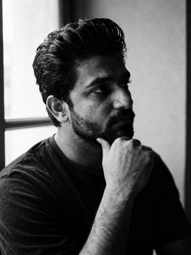 Stark black and white portrait of Samir Singh in deep thought, dramatic side-lit window light, high contrast, rich paper textures, 35mm film grain.