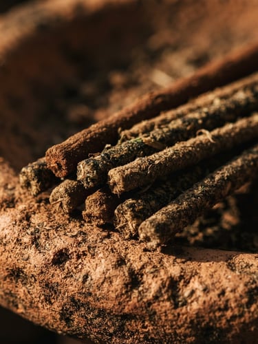 Macro close-up of hand-rolled incense sticks resting on a terracotta surface, warm side-lighting, deep shadows, 35mm