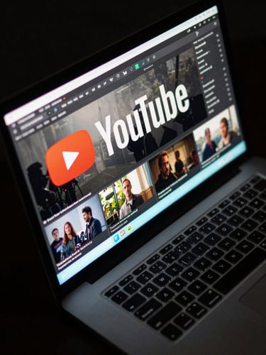 Tight overhead shot of a laptop screen displaying a cinematic YouTube thumbnail in progress — bold title text, high-contrast lighting split, dark studio environment with a single cyan monitor glow illuminating the keyboard edge