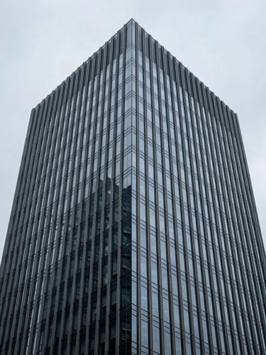 Low-angle architectural shot of a modern glass skyscraper facade against a cool overcast sky, sharp reflections, minimal composition, 35mm