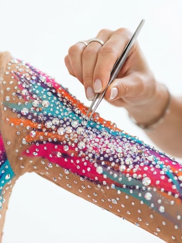 Close-up of designer Ira hand-placing crystals on a vibrant mesh leotard sleeve under bright studio light, 85mm lens, shallow depth of field