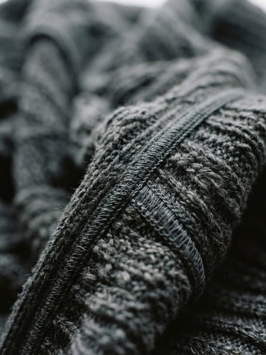 Extreme close-up of charcoal heavy-gauge technical knit fabric in motion, soft overcast window light, showing architectural drape and sharp seam details, 35mm