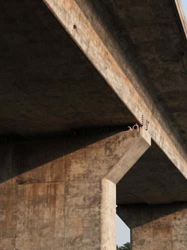 Wide architectural shot of a cantilevered concrete bridge structure in low-key warm lighting, deep shadows, emphasizing tension and connection.