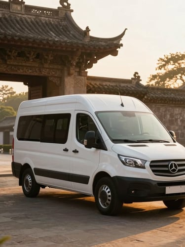 A clean, modern white family van parked near a historic stone temple gate at sunrise, warm golden light casting long soft shadows