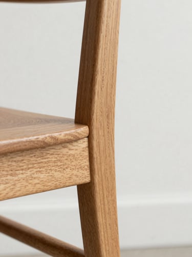 Close-up of a finished teak dining chair corner joint, natural grain visible under even north-facing daylight, white wall background, no tableware or styling props