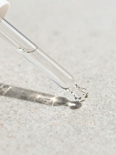 Macro close-up of a minimalist clear glass peptide dropper bottle on a clean, light grey stone surface, bright natural daylight, soft shadows, sharp focus