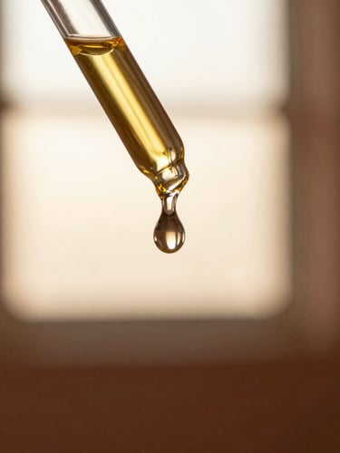 Macro close-up of a single golden oil droplet falling from a heavy glass dropper, soft golden-hour window light, warm terracotta background, shallow depth of field