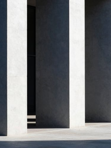 Minimalist architectural photography, clean concrete pillars casting long rhythmic shadows in bright daylight, sharp contrast, navy tones, 35mm lens
