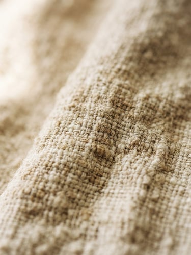Close-up of soft organic linen texture, warm beige and ivory tones, diffused morning light, shallow depth of field.