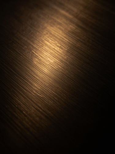 Close-up of a dark steel and brushed gold texture, low-key lighting, warm golden-hour accents, abstract and sophisticated.