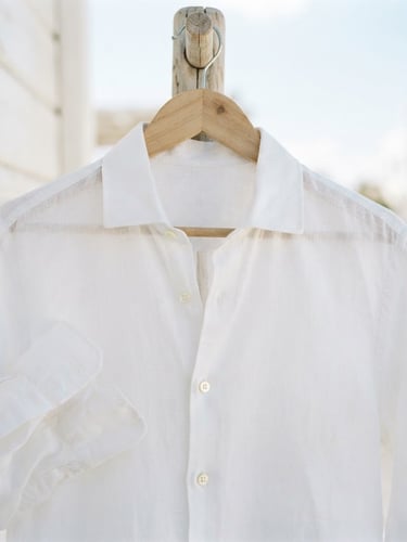 Close-up of a crisp white linen shirt on a natural wooden hanger, bright high-key coastal daylight, shallow depth of field, 35mm