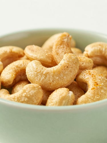Macro shot of golden roasted cashews seasoned with sendha namak in a minimalist sage green ceramic bowl, soft side light, premium food photography
