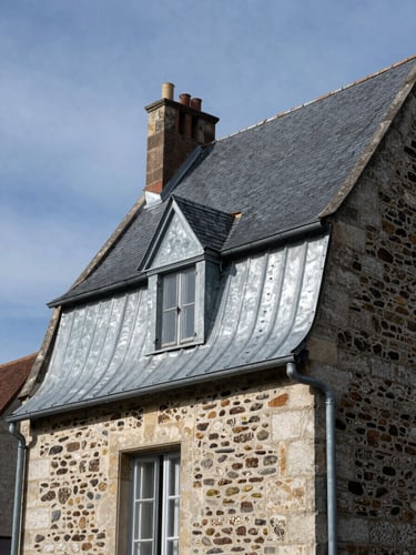 Détail d'une gouttière en zinc neuve parfaitement posée le long d'une corniche en pierre de taille d'une maison meulière, ciel clair du Val-de-Marne