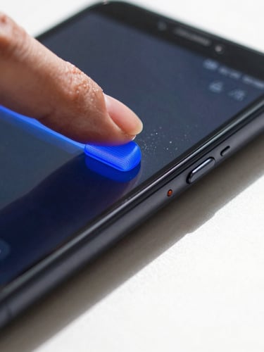 Extreme close-up macro shot of a thumb sliding a bright blue volume slider on an Android phone, casting a sharp shadow onto a white desk.