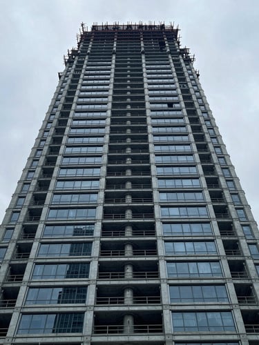 Low-angle heroic shot of modern architectural steel and concrete skyscraper under construction, cool overcast daylight, desaturated slate blue tones, sharp focus, 35mm lens