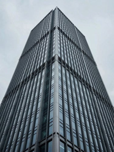 Low-angle heroic shot of a modern skyscraper's steel and glass facade under a cool, overcast sky, sharp architectural angles, desaturated blue and slate tones, editorial architectural photography, 35mm lens, sharp focus.