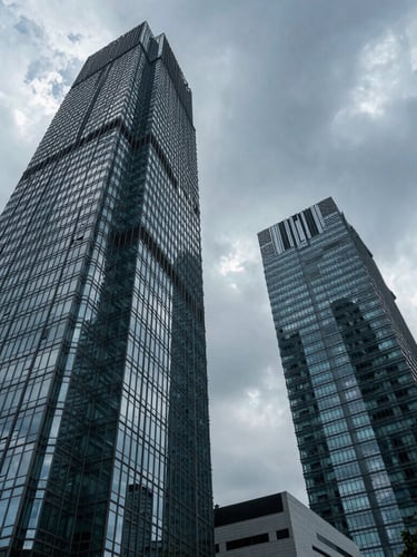 Low perspective wide-angle shot of high-end corporate glass towers in Jakarta under cool-toned dramatic overcast sky, sharp architectural lines.