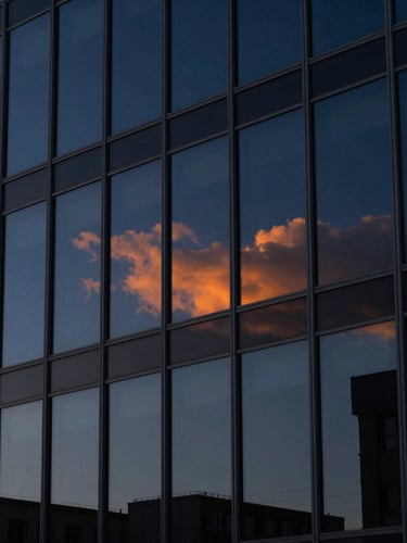 Extreme close-up of a modern architectural glass facade reflecting deep navy blue sky with a sharp orange sunset light leak, highly structured grid lines, dramatic shadows, editorial corporate photography style.