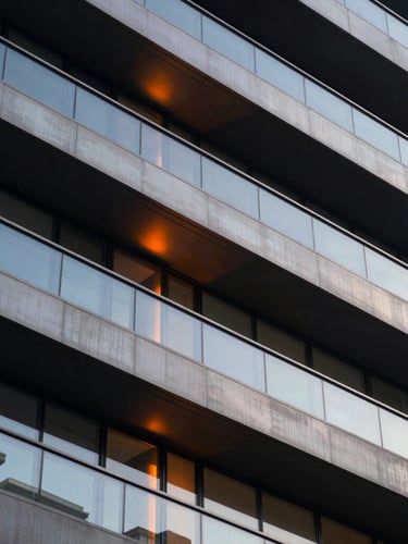 Extreme close-up of structured architectural lines in dark steel and glass, warm orange light leak reflecting on clean metallic surface, sophisticated corporate photography, 35mm lens