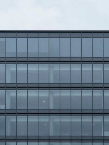Minimalist architectural photography of a modern glass and steel facade, desaturated blue and slate tones, cool overcast daylight, sharp focus