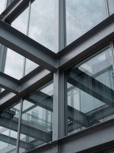 Tight abstract architectural crop of structural steel beams and glass panels, sharp overcast shadows, desaturated slate tones, 35mm