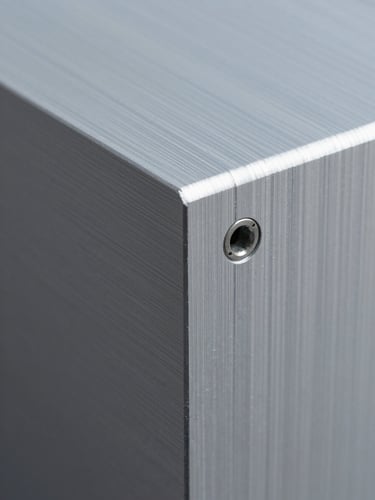 Extreme close-up of a fabricated aluminium composite panel edge, mounting bracket visible, crisp machined corner under cool studio daylight, surface texture sharp and dimensional