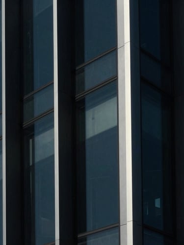 Minimalist architectural glass facade in Padova, sharp linear patterns, deep navy and black shadows, crisp white reflections, cinematic 35mm lens.