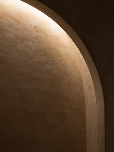 Close interior detail of a curved architectural recess, warm ambient light pooling along a smooth plaster wall from a concealed source at upper left, deep shadow falling to the lower right, no people, minimal and spatial