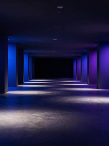 Full-bleed immersive event space captured from within during a live branded installation, dramatic directional lighting casting long shadows across the floor, spatial depth extending in all directions from the center, deep blue and violet ambient tones, no people