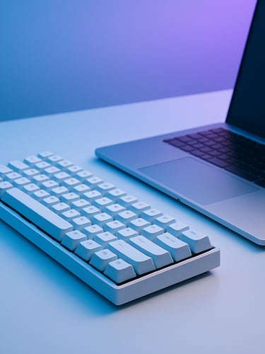 Minimalist workspace with a mechanical keyboard, clean aluminum laptop, soft cool blue and violet ambient light from a screen off-camera, sharp focus, 35mm