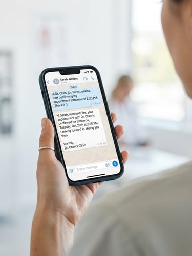 Close-up of a mobile phone screen showing a WhatsApp chat interface with a patient confirming an appointment, clean white background, soft natural daylight, over-the-shoulder shot