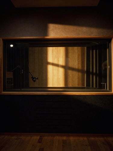 Moody cinematic wide shot of an empty premium recording studio in Berlin at golden hour, amber sunlight cutting through the window onto dark wooden panels and acoustic diffusers, 35mm film.