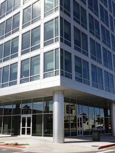Wide-angle architectural view of a modern steel and glass commercial office building in Lehi, Utah, under bright daylight with sharp geometric shadows.