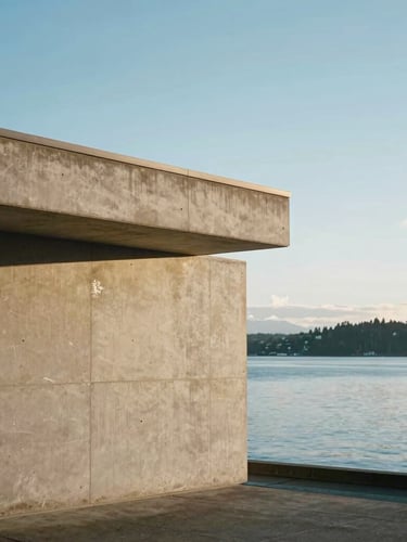 Diffused Pacific Northwest daylight illuminating a clean architectural concrete structure on Bainbridge Island, water reflecting cool sky blue tones in the background, minimalist composition with generous negative space.