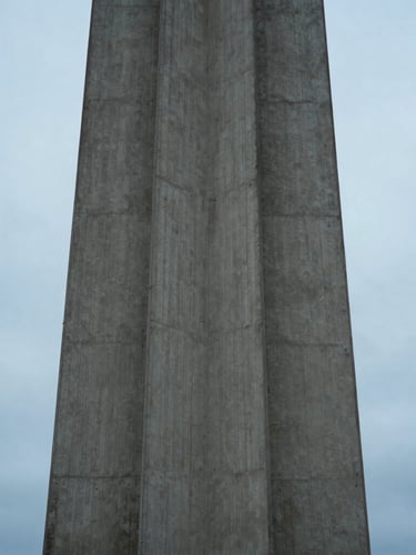 A tall architectural structure on Bainbridge Island, clean concrete lines meeting an overcast sky blue horizon, diffused cool light, portrait orientation.